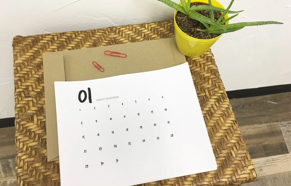 The January calendar printable laying on a tablet next to a potted plant. 