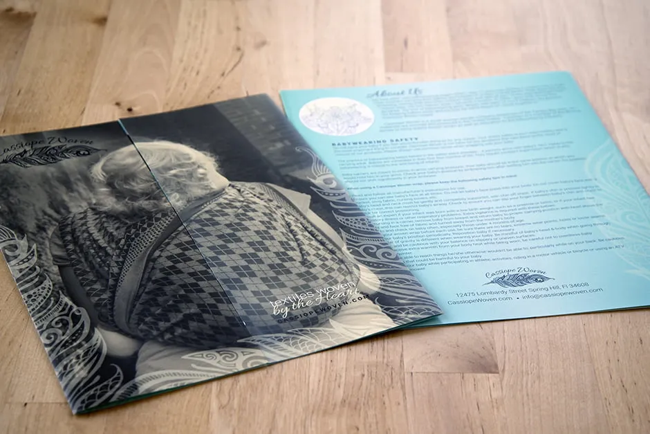 A print brochure for Cassiope Woven. The front cover is of a small child on his mother's back wrapped with a babywearing cloth. 