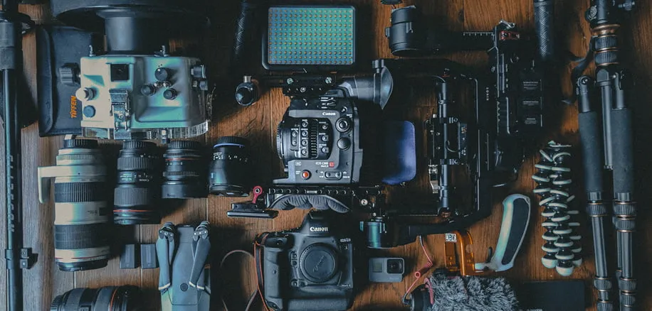 Camera equipment, including lenses and tripods, lay across a wooden table. 