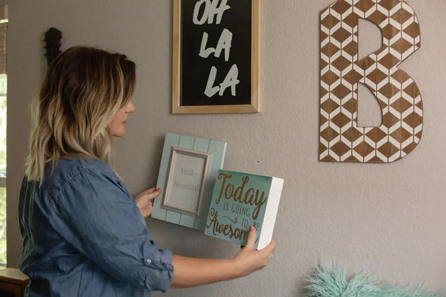 Deidra, the founder of Heart and Home Makeovers, hangs a picture frame and a canvas sign on a family's wall of their newly-decorated home. 