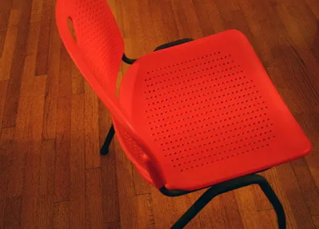 A red chair with rows of small holes on it. 