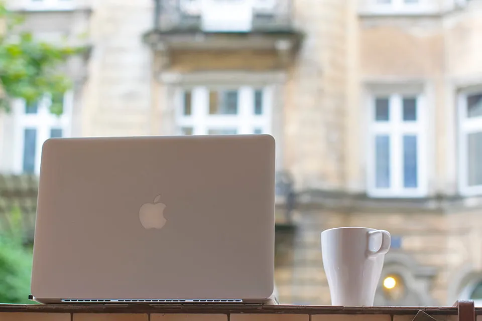 A Macbook computer sitting on a table with a white coffee cup next to it. 