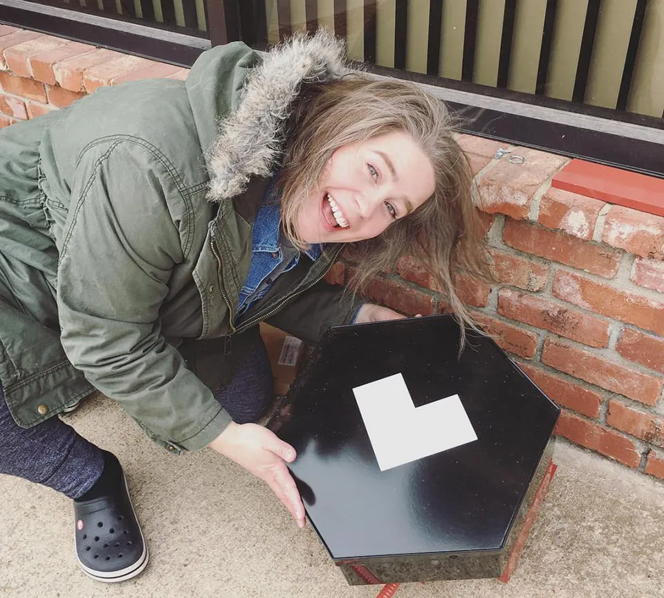 Amy bends down and holds a part of the myheartcreative outdoor sign before it is hung outside. 