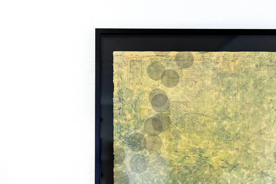 A corner of an abstract piece by artist Emma Difani. The piece's frame is black and the painting has subtle yellow, green, and grey colors. 