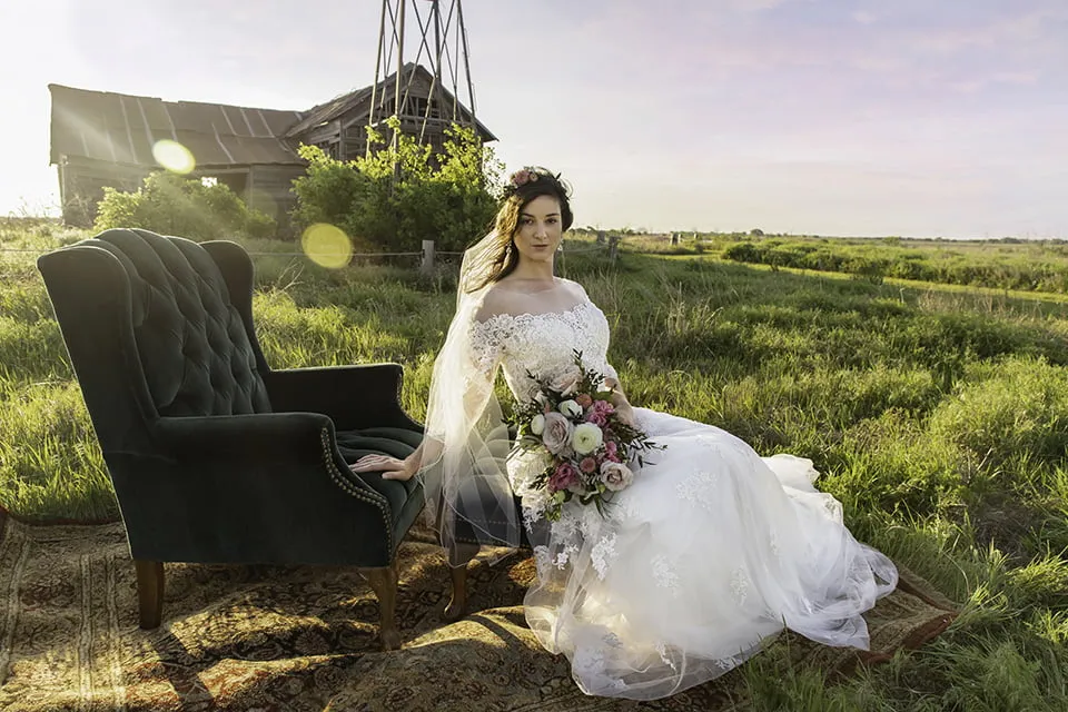 The bride sits with her flower bouquet in hand. She is sitting on a rig next to a dark green velvet chair. 