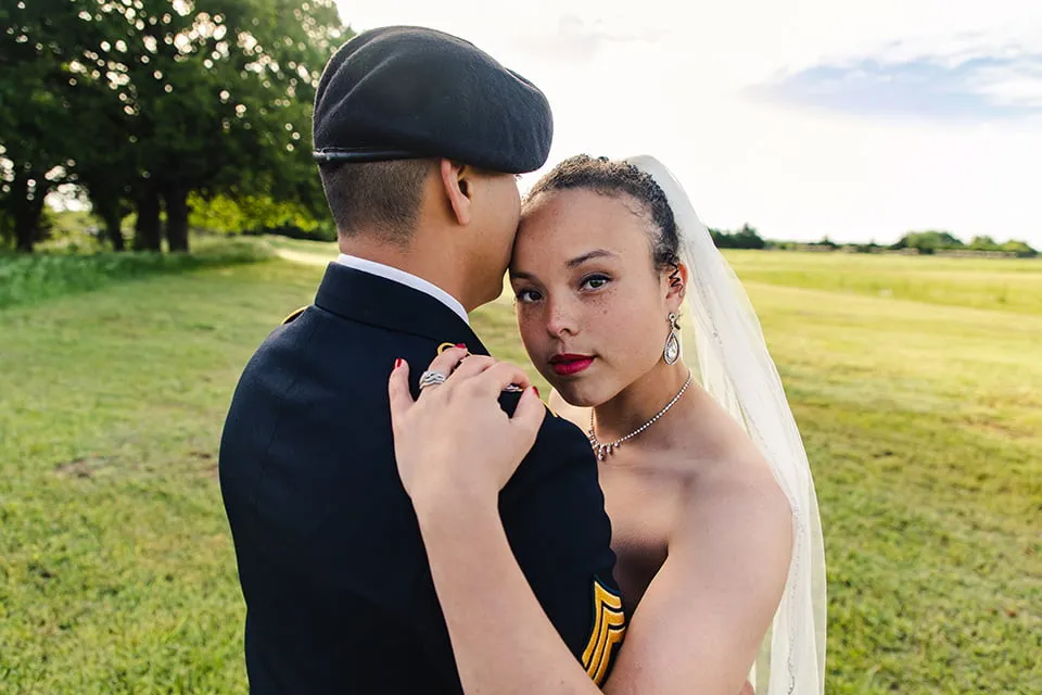 The bride hugs the groom while standing in a field. 