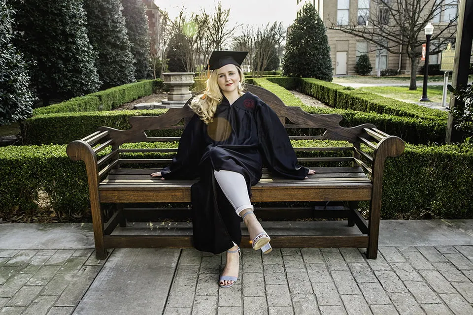 An image of a graduate sitting on a bench in her cap and gown. The image is correctly exposed, so the subject is well-lit and easily seen. 