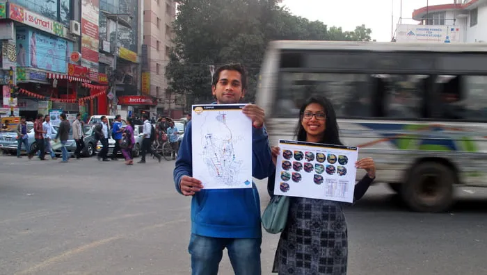 A man and a woman hold a bus map while standing in front of a busy street in Dhaka. 