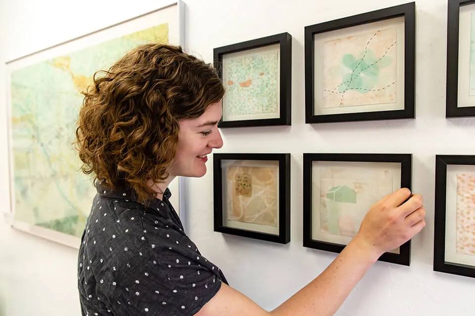 Artist Emma Difani smiles while adjusting one of the frames in the gallery wall of her artwork at the studio. 