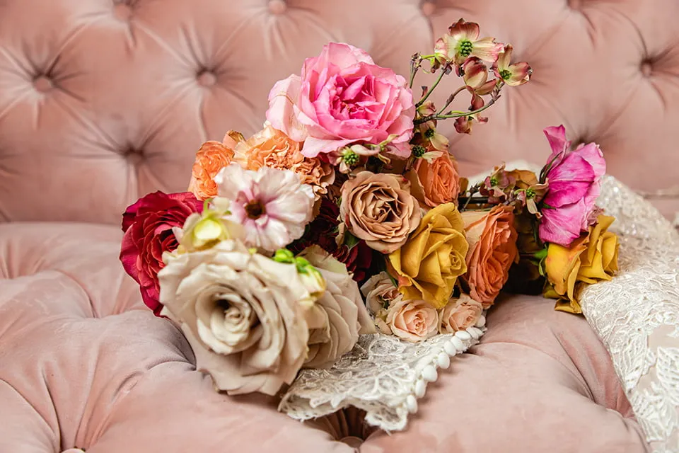 An up-close shot of the bride's wedding bouquet as it lays on a pink tufted sofa.