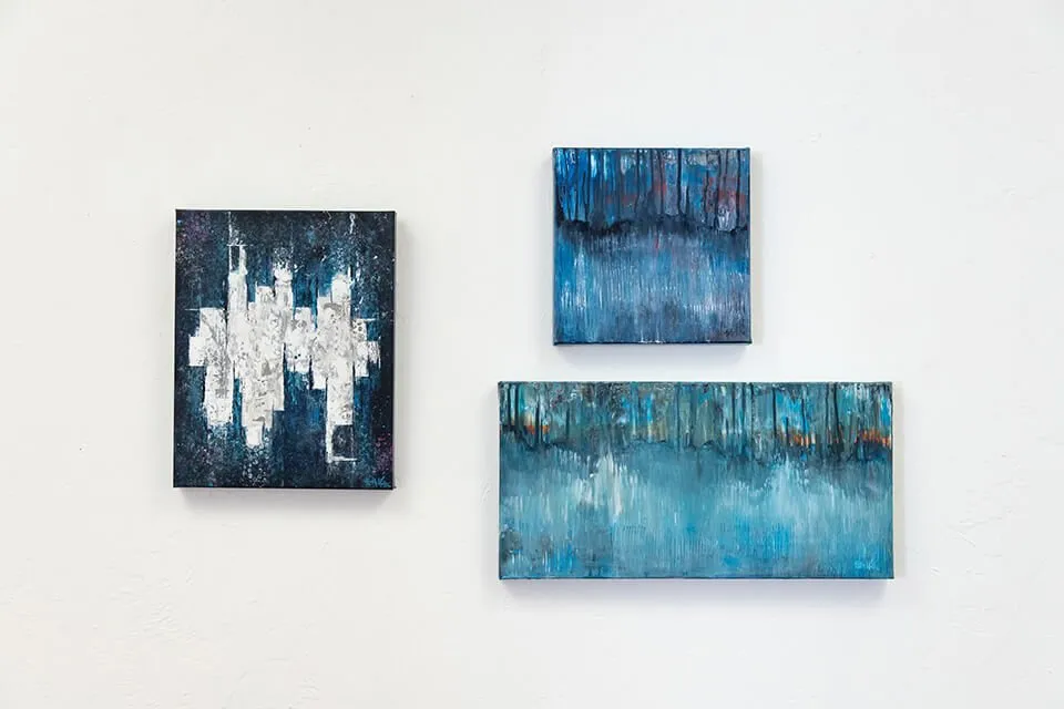 A gallery of three abstract paintings by Keith Wolfe hanging on the wall at the myheartcreative studio. All three paintings have a blue-centered color palette. 