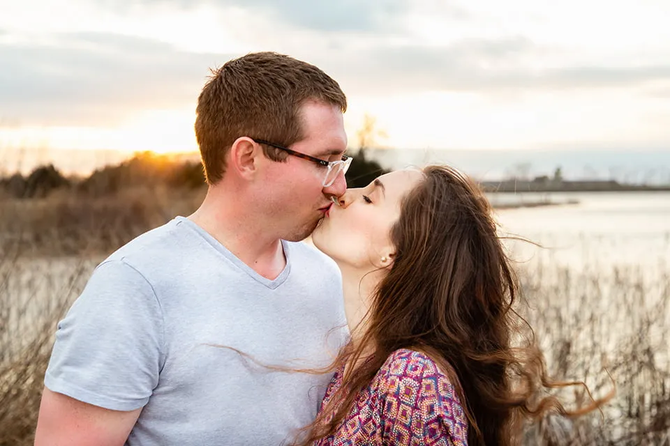 A young couple share a kiss in a field at sunset. 