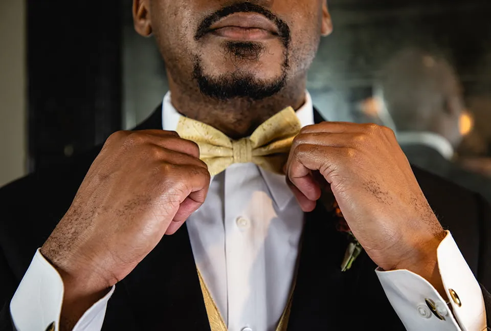 The grom adjusts his gold bow tie. 