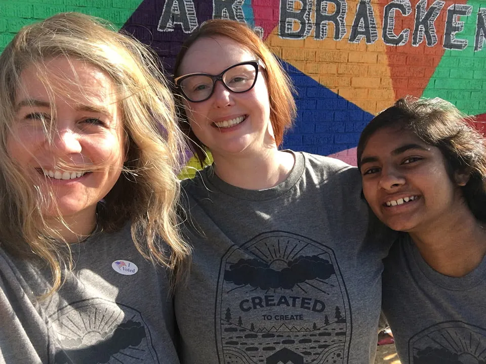 Amy, April, and Kaitlyn smile for a photo while standing in front of a colorful mural. 