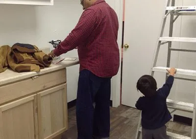 Amy and Sam's toddler, Maximus, grabs a rung on the ladder while Sam puts together the new studio kitchen cabinets.