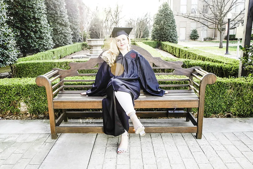 An image of a graduate sitting on a bench in her cap and gown. The image is overexposed, so the subject appears too bright. 