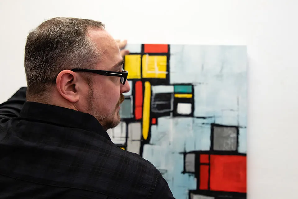 Artist Keith Wolfe holds his abstract painting "Reconstruction." He gazes to the right. 