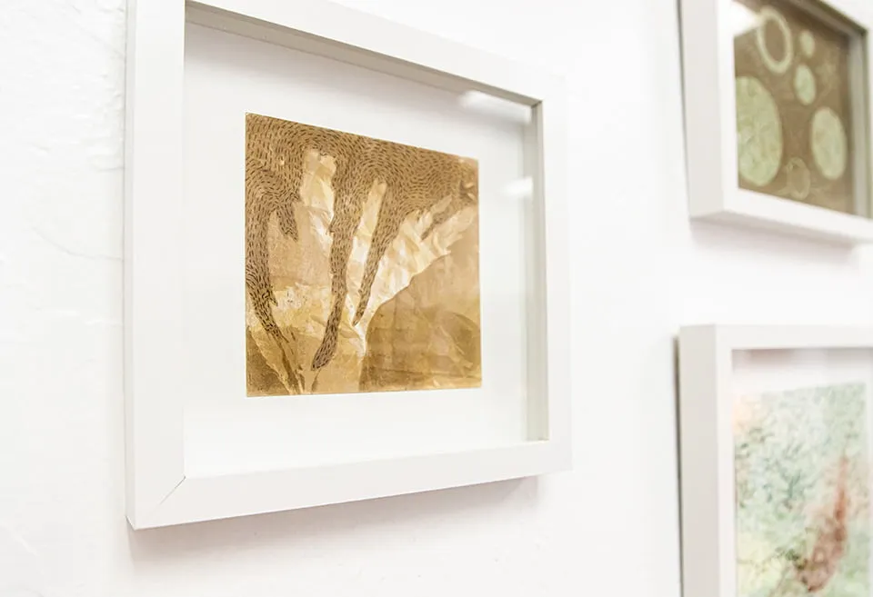 A abstract piece by Emma Difani in a white frame. The piece is located next two two others on a gallery wall at the studio. 