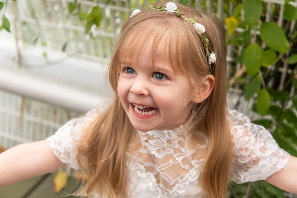 An image from the Taylor family's Oklahoma photoshoot of the young daughter. She is smiling while wearing a white lace dress and a flower headband. 