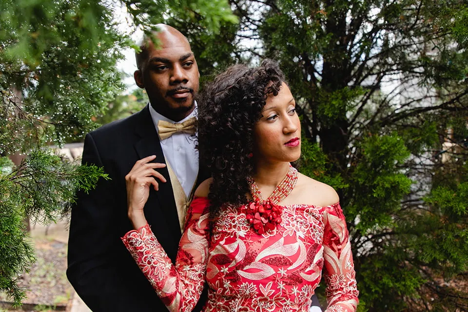 The bride gazes to the left while standing in front of the groom. She is wearing a custom red dress from Nigeria. 
