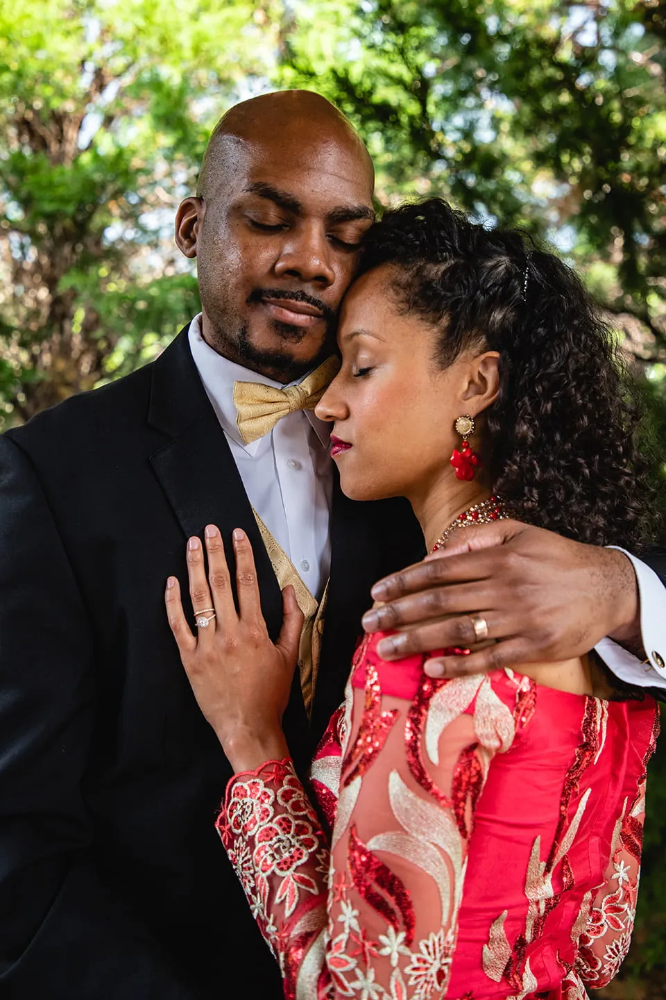 The bride closes her eyes and hugs the groom while placing her hand on his chest. The groom closes his eyes and embraces his bride. They are standing amongst trees at Rose Briar Place. 