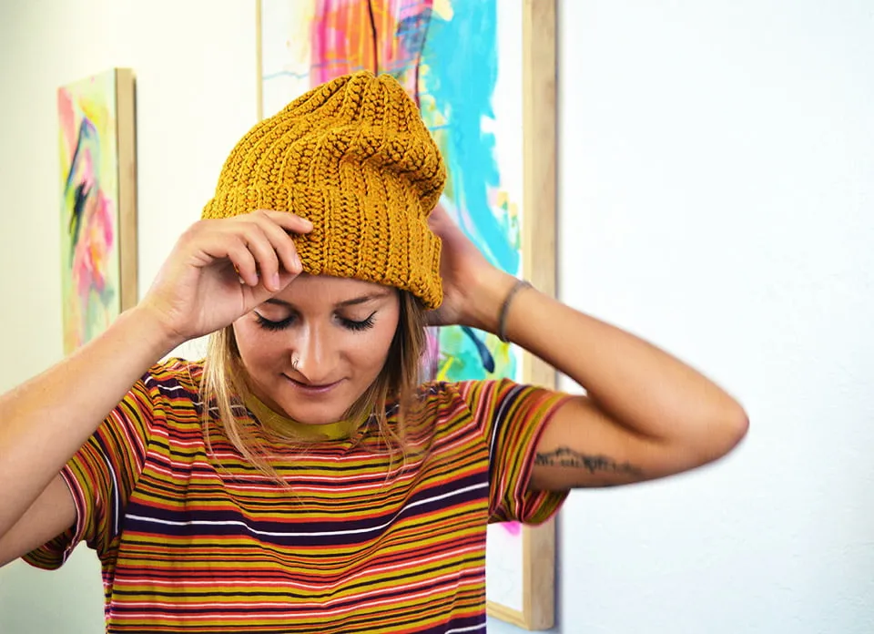 Artist Virginia Sitzes adjusts her yellow beanie while walking by her paintings at the studio. 