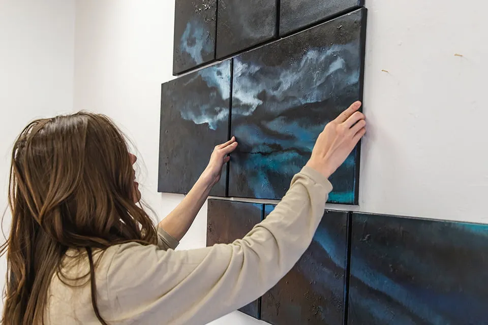 The Nature of Abstract - myheartcreative Artist Wendi O'Connor places an abstract painting on the studio wall as a part of a large gallery. The painting is a blue and black abstract piece.
