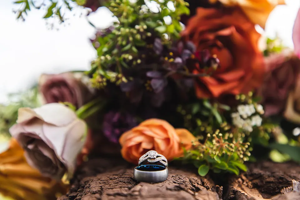 The bride and groom's wedding bands sit on a wood log with the bridal bouquet in the background. 