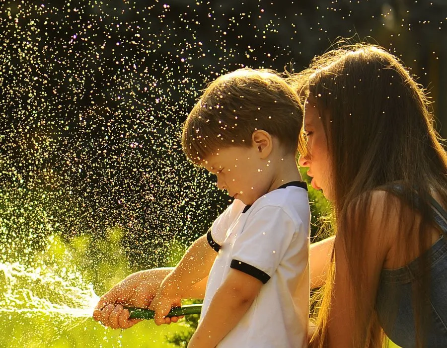 An image of a mom and young son playing with water coming from a water hose. 