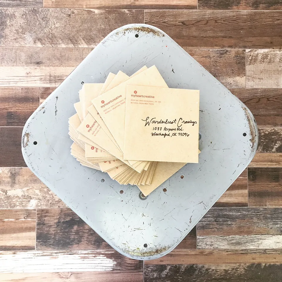 A stack of holiday cards from myheartcreative sitting on a grey stool. The envelopes are a light brown color. 