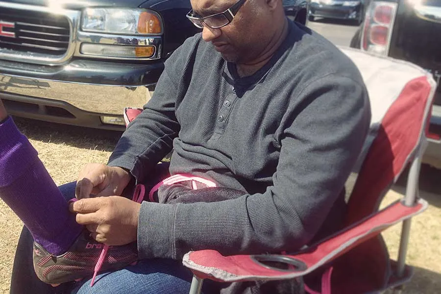Sam sits in a lawn chair and ties his daughter's soccer cleats. 