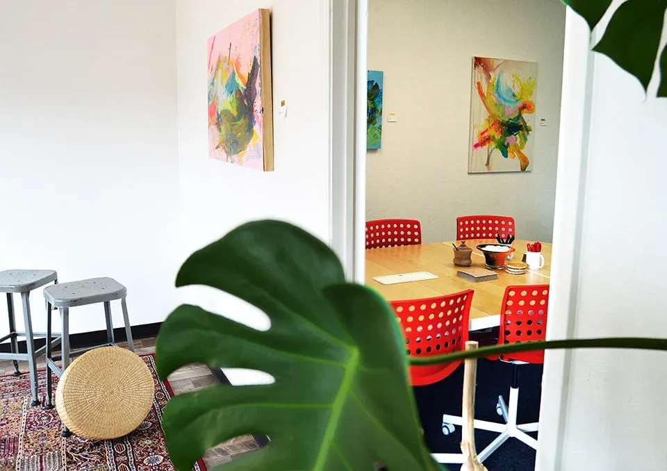 A shot of the doorway from the back sitting area of the studio to the conference room. Multiple paintings by Virginia Sitzes are hanging on the walls. 