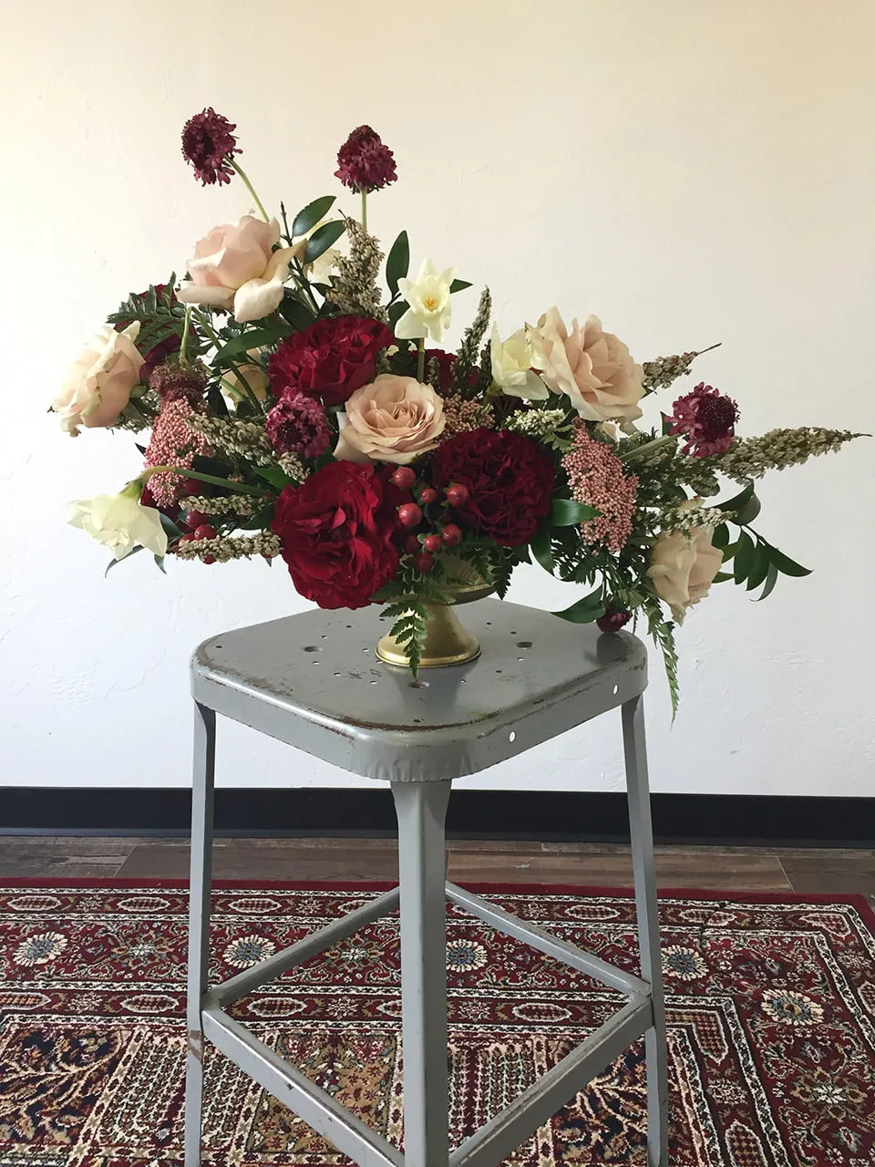 A large flower arrangement by Crooked Roots. The bouquet has dark red and light pink flowers throughout. 