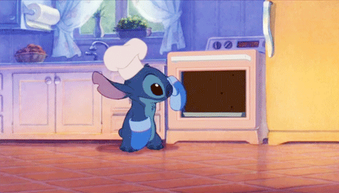 A gif showing Stitch from "Lilo and Stitch" removing a large chocolate cake from an oven. 