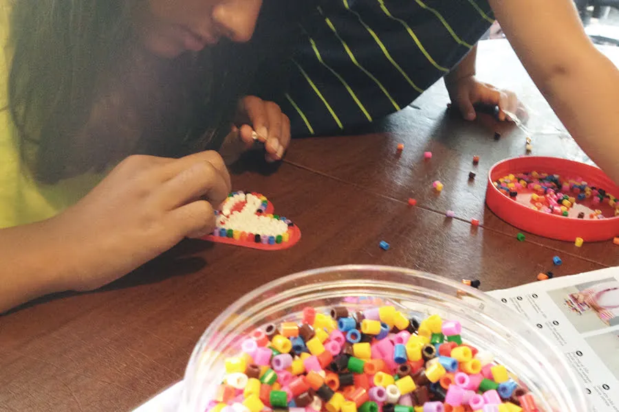 A young girl places colorful beads in the shape of a heart for an art project. 
