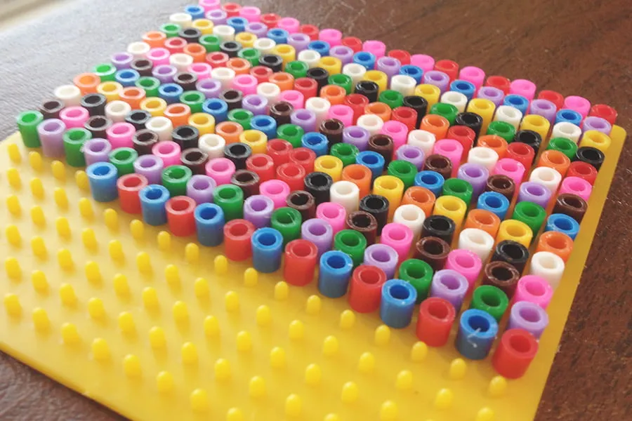 Rows of multicolored beads on a yellow bead organizer. 
