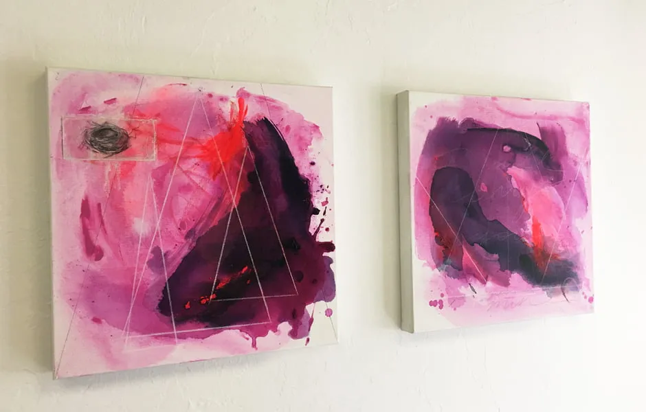 Two abstract paintings by Brandi Downham hang on the studio wall. Both paintings have pink, purple, and red colors. 