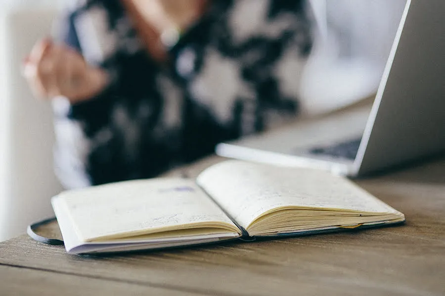 How to Be a Rockstar Remote Worker in a World of Employees - myheartcreative A calendar book resting on a woman's desk as she works.