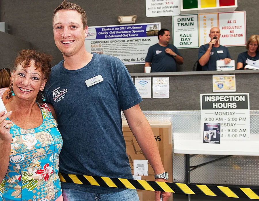 Louisiana's 1st Choice Auto Auction - myheartcreative A LAFCAA employee smiles with a woman holding an auction ticket in her hand. The auctioneer talks in the microphone behind them.