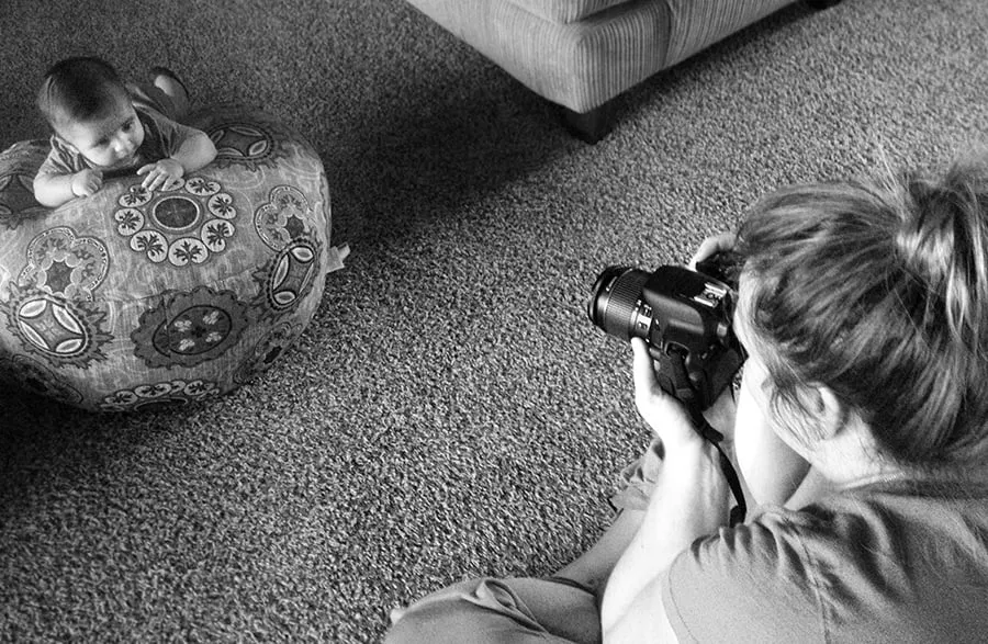 Baby Bubba's Tummy Shoot - myheartcreative Ashley, Maximus's aunt, uses a professional camera to take photos of Maximus. She sits with her legs crossed in the floor, while he rests on a patterned pillow.