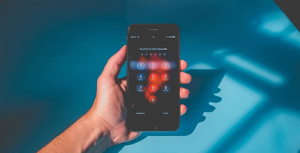 A hand holding an iPhone showing "Touch ID or Enter Passcode" screen. 