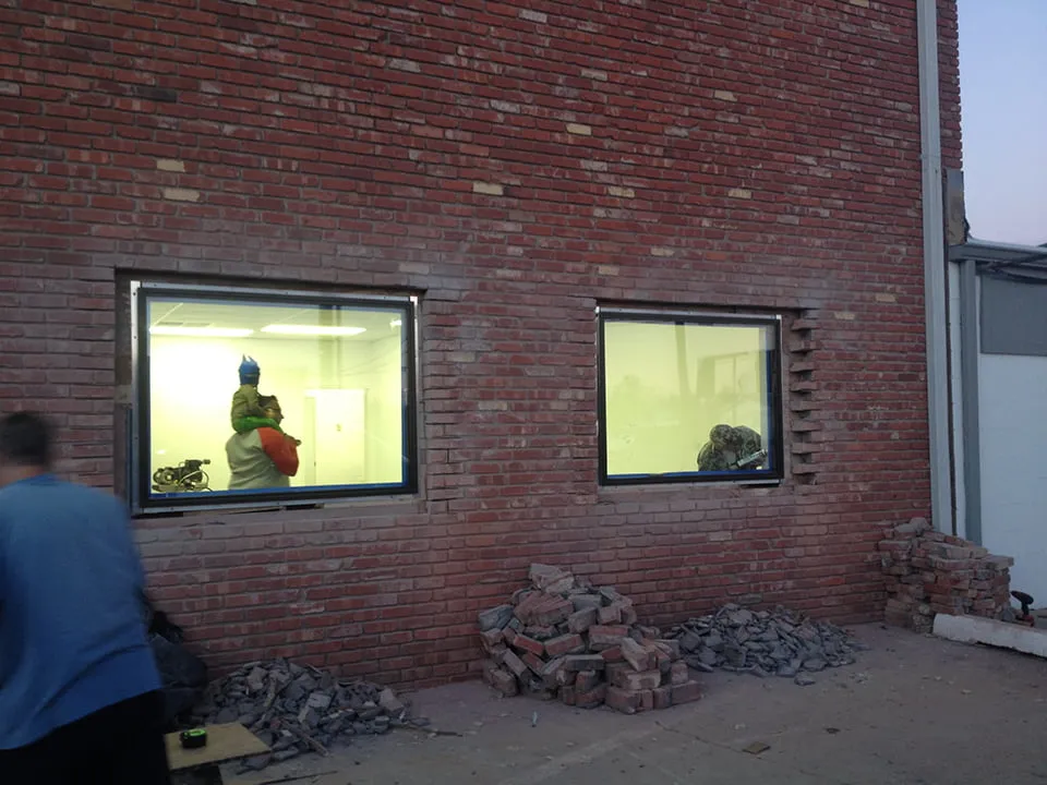 Sam is seen through a window with his son on his shoulders as he walks through the new myheartcreative studio. There are piles of bricks outside of the building. A worker is seen caulking the new windows. 