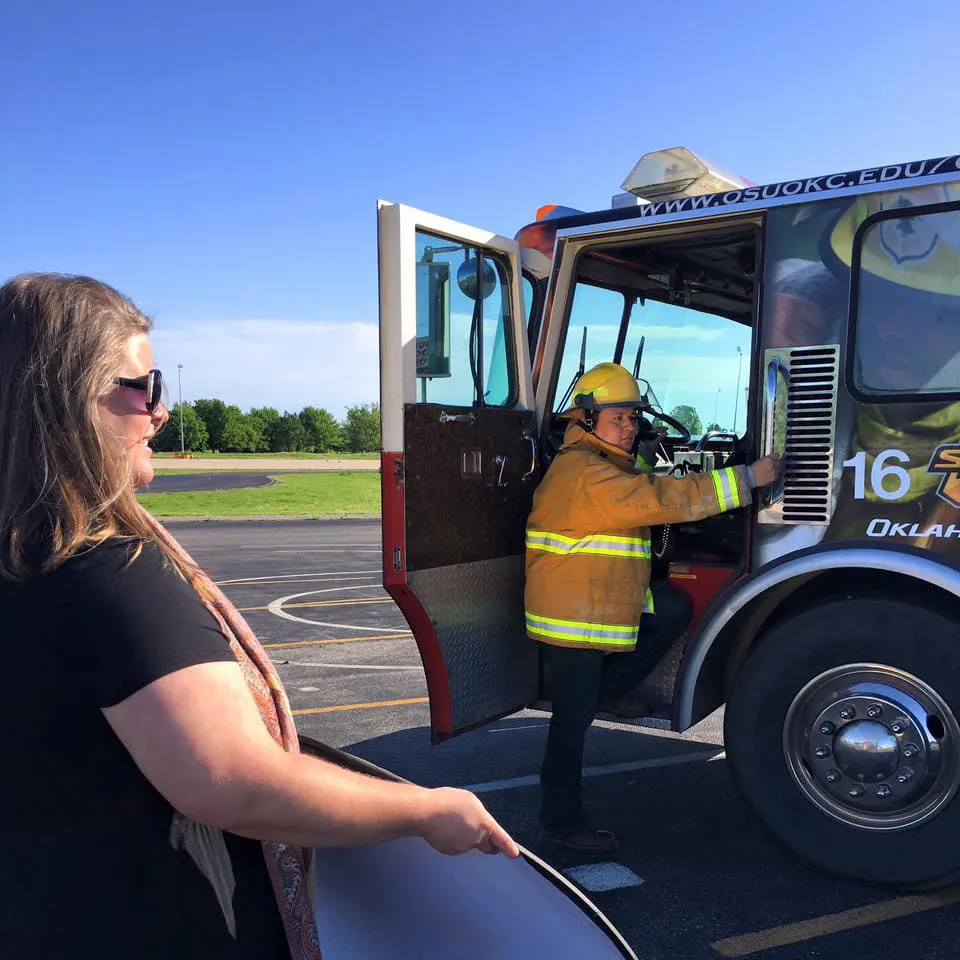 Amy shining a light reflector on a firefighter getting into a firetruck at a photoshoot. 