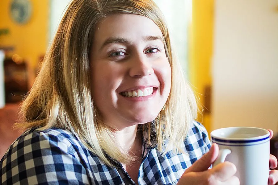 Amy holding a white coffee cup and smiling excitedly. 