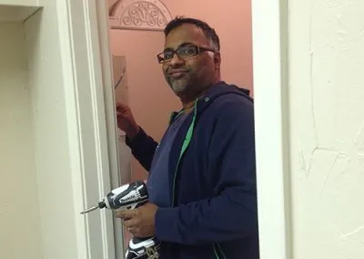 The Operations Director, Sam, uses a screw gun to hang up the paper towel holder in the new studio bathroom.
