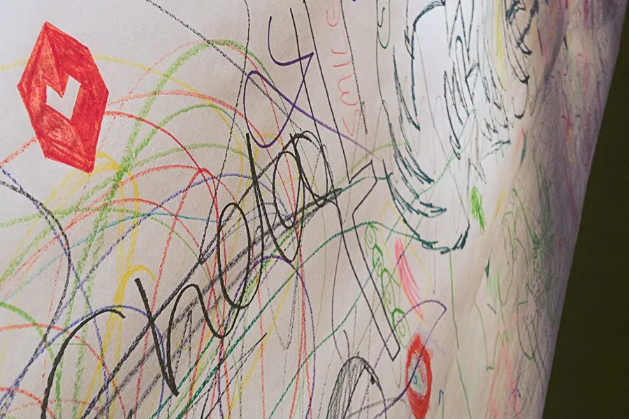 A white wall with multi-colored scribbles all over it. The myheartcreative logo is hand-drawn in the top corner. 