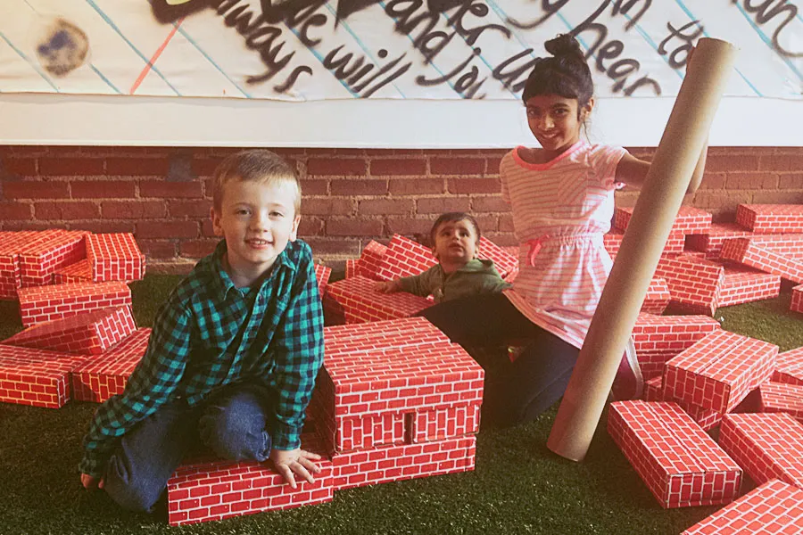 A young girl, a young boy, and a toddler play amongst foam bricks in a creative play space. 