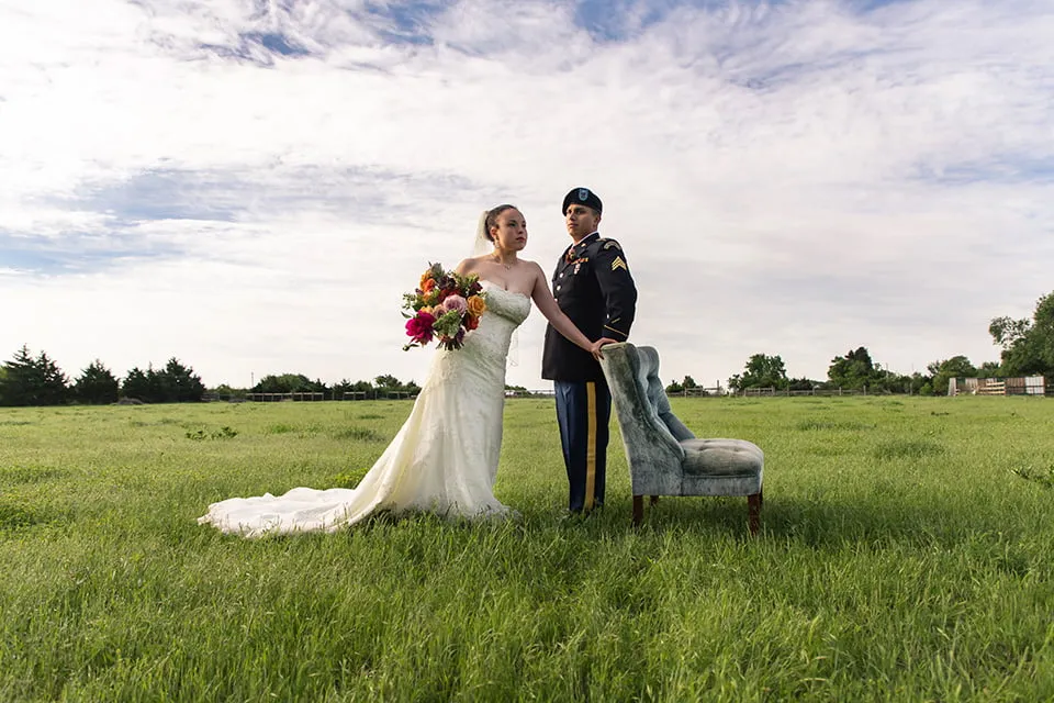The bride and the groom gaze off into the distance while resting one arm on a grey velvet chair. 