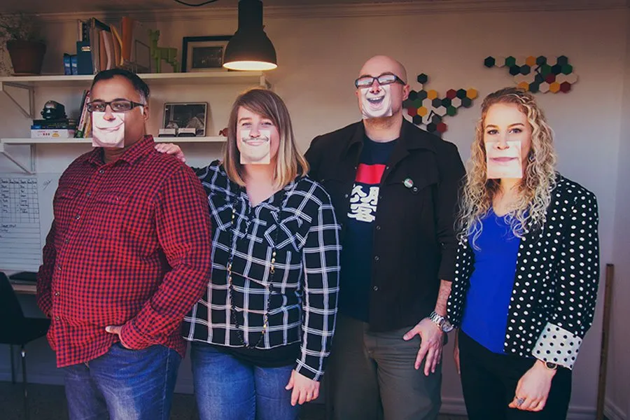 Amy and Sam pose with two clients in the new home studio. All four are wearing funny pictures of mouth expressions over their faces. 