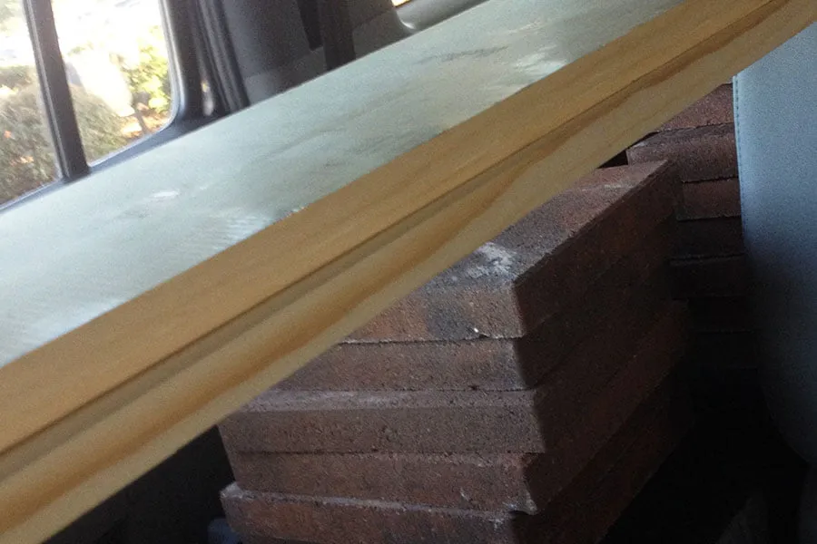 Two wooden boards sit on top of a large stack of pavers. 